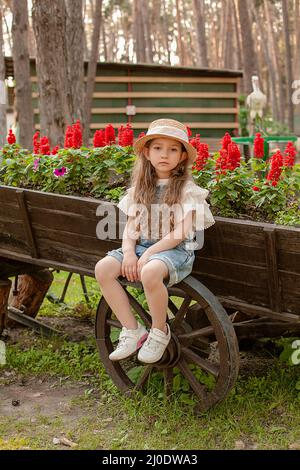 Préadolescence fille assise sur la roue de chariot rustique en bois utilisé comme lit de fleur dans le parc de la ville Banque D'Images