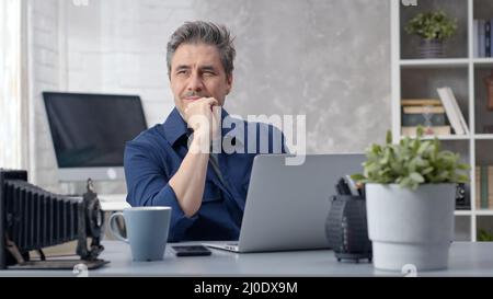 Homme barbu travaillant en ligne avec un ordinateur portable à la maison assis au bureau. Homme d'affaires dans le bureau à la maison, la navigation sur Internet. Portrait de l'homme adulte moyen, d'âge mûr, en 50s. Banque D'Images