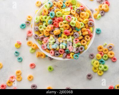 Sur fond blanc, anneaux de céréales aux fruits multicolores. Vue grand angle. Petits déjeuners rapides à grains entiers, mets sucrés. Enfants, nourriture de régime. Supermarché Banque D'Images