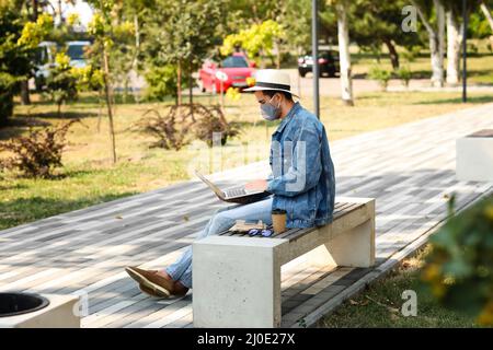 Jeune homme avec masque médical utilisant un ordinateur portable sur banc dans le parc Banque D'Images