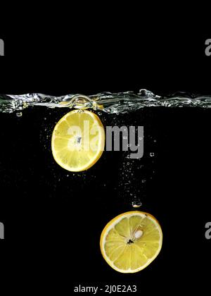 citron tranché tombant dans l'eau sur fond sombre. Vue sous l'eau. Cuisine, végétarien, cuisine à la maison concept Banque D'Images