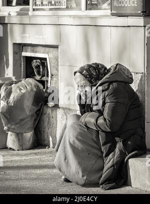 Bucarest, Roumanie - 02.04.2022: Portrait d'une vieille femme solitaire assise sur le trottoir dans le centre de Bucarest. Banque D'Images