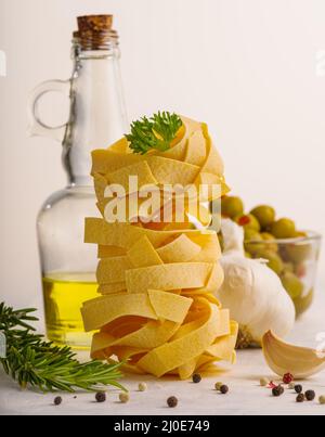 Prise de vue macro. Pâtes italiennes, nouilles, huile d'olive, ail, herbes, olives vertes dans un bol sur fond blanc. Cuisine italienne. Restaurant, hôtel, café. Banque D'Images