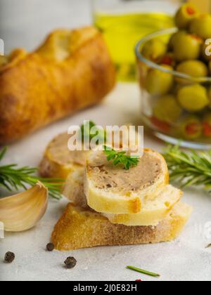 Gros plan. Sandwiches à la baguette de foie gras français garnis de feuilles de persil, d'olives vertes, de baguette et de romarin sur fond blanc. Festiv Banque D'Images