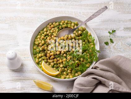 Ragoût de pois chiches dans une sauce verte avec persil et citron sur fond de bois blanc, style rustique, vue sur le dessus. Délicieux repas sains faits maison Banque D'Images