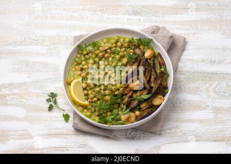 Soupe de pois chiches dans une sauce verte avec aubergines cuites au four, persil et citron sur fond de bois blanc, style rustique, vue de dessus. Maison délicieuse et saine Banque D'Images