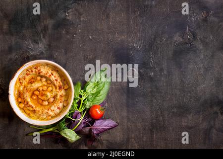 L'hoummos sur une plaque avec des tomates cerise et d'herbes sur un fond de bois foncé Banque D'Images