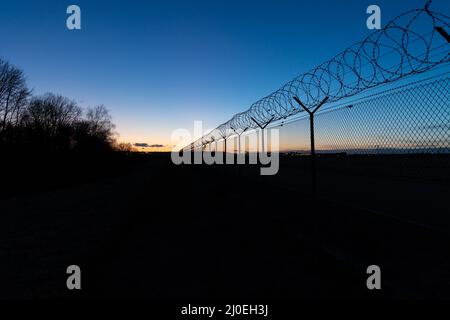 vue le long d'une grande clôture avec fil barbelé contre le ciel bleu et coloré du coucher du soleil. pas de nuages. Aéroport Stuttgart Banque D'Images