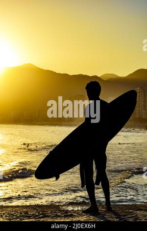 Surfeur silhouette avec sa longue planche à voile regardant la plage d'Iapnema Banque D'Images