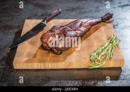 Jambe d'agneau fumée sur une planche de bois avec un couteau Banque D'Images