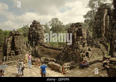 Les visiteurs ayant du temps de visite sous les tours en pierre géantes sculptées avec des visages souriants à Prasat Bayon (temple de Bayon) à Angkor Thom, le centre de l'ancienne ville angkorienne qui était la plus grande et la plus peuplée ville du monde où vivaient jusqu'à 900 000 personnes, jusqu'à ce que les guerres et la catastrophe climatique en 14th et 15 siècles l'avaient forcé à être abandonné. Crédits: PACIFIC Imamica/Alamy Banque D'Images