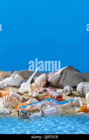 Une bouteille en verre avec une lettre lavée sur la plage. Plage de mer pleine de coquillages et de sable. Ciel bleu. De l'eau propre. Banque D'Images