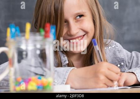 La fille résout la tâche donnée dans la salle de classe. L'écolière écrit diligemment dans un bloc-notes. Banque D'Images