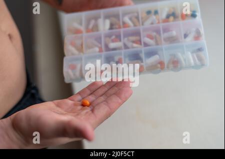 Gros plan d'une paume mâle avec des pilules.Un homme prend une dose quotidienne de vitamines et de suppléments nutritionnels d'une boîte quotidienne de pilules. Banque D'Images