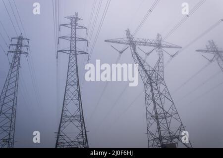 Des pylônes de puissance électrique qui disparaissent dans un paysage de brouillard épais Banque D'Images