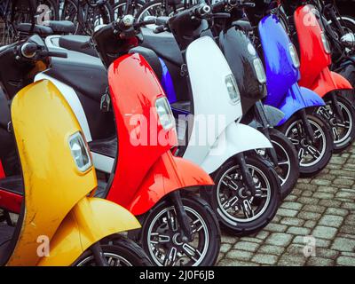 Les cyclomoteurs électriques multicolores sont en rangée sur des pavés Banque D'Images