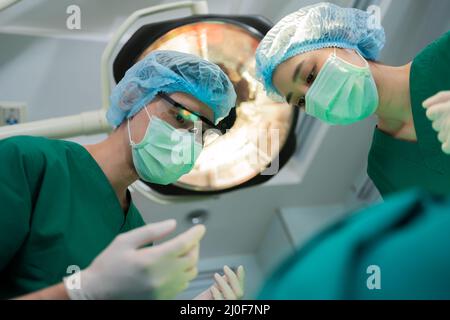 Prise de vue à angle bas de l'équipe de chirurgiens professionnels effectuant la chirurgie en salle d'opération, chirurgien, assistants, et infirmières effectuant la chirurgie sur un patient, He Banque D'Images