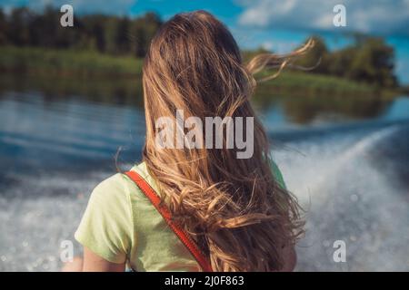 Une jeune femme aux cheveux longs fait un bateau rapide sur la surface de l'eau du lac. Vue arrière. Sur le fond d'un blanc FO Banque D'Images
