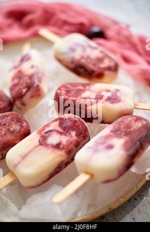 Crème fraîche et cerise des popsicles faits maison placés sur une plaque de céramique blanche avec des fruits et du textile Banque D'Images