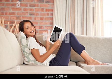 Sa tablette numérique est toujours à portée de main. Portrait d'une jeune femme attrayante utilisant une tablette numérique tout en étant assise sur le canapé. Banque D'Images