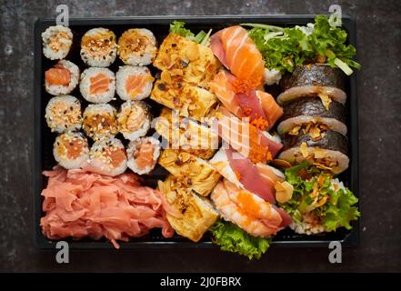 Gros plan de divers ensembles de sushis dans une boîte de livraison en plastique noir. Vue de dessus Banque D'Images