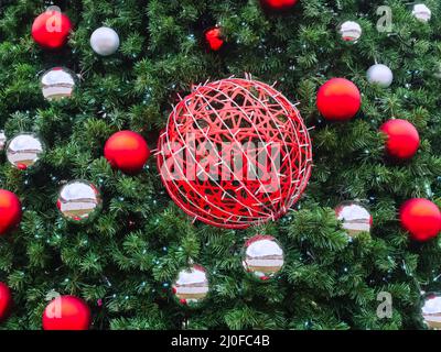 Une boule en osier rouge enorée d'une guirlande est suspendue les branches d'épinette avec de petites boules rouges et argentées autour Banque D'Images