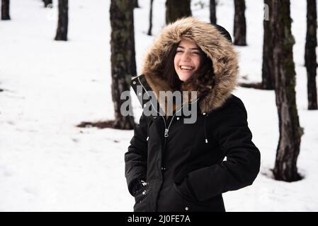 Jeune fille adolescente heureuse et belle vêtue de vêtements d'hiver debout sur la neige et souriante. Banque D'Images