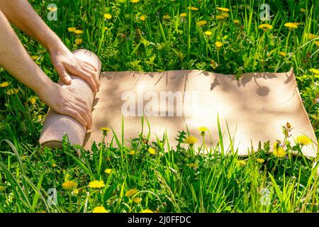 Homme roulant son tapis après un cours de yoga sur une prairie verte, un jour ensoleillé d'été, foyer sélectif Banque D'Images