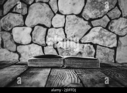 Ouvrez le vieux livre sur une ancienne table en bois sur un fond de murs en pierre. Attention sélective, pho noir et blanc Banque D'Images