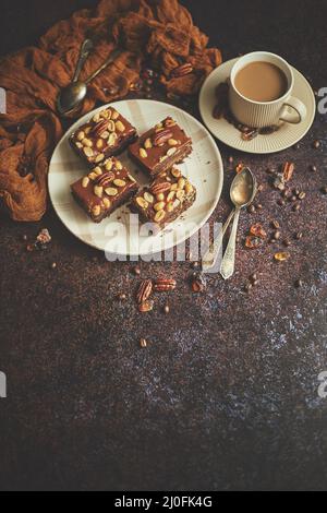Les morceaux carrés de délicieux gâteau au caramel avec des arachides et noix du brésil servies avec du café au lait Banque D'Images