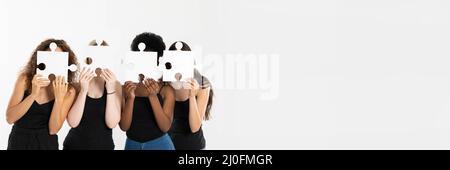 Dans un cadre panoramique, quatre jeunes filles tiennent des puzzles dans leurs mains, couvrant leur visage pour devenir anonyme et montrer qui diffèrent Banque D'Images