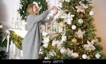 Bonne jeune femme blonde décorant arbre de noël avec boule à sa maison Banque D'Images