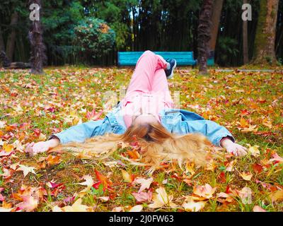 REDHEAD fille est avec ses jambes croisées dans un parc sur une prairie parsemée de feuilles d'automne Banque D'Images