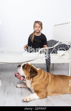 Le Bulldog anglais est gardé par son fidèle défenseur par le lit de la petite fille. La fille et son animal de compagnie à quatre pattes. Banque D'Images