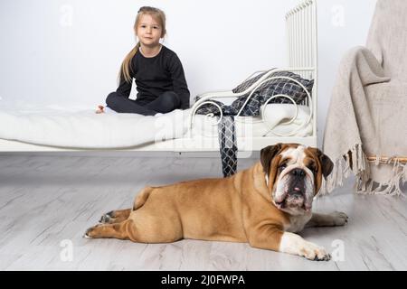 Le Bulldog anglais est gardé par son fidèle défenseur par le lit de la petite fille. La fille et son animal de compagnie à quatre pattes. Banque D'Images