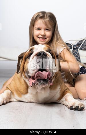 Une jeune fille dans une chambre, assise sur le sol avec son chien et le caressant. Enfant et chien. Le Bulldog anglais est un pur revin Banque D'Images