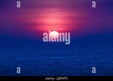 Magnifique coucher de soleil sur la mer, vue de la plage. Soleil rond et lumineux au crépuscule sur une mer calme avec un ciel sombre et flou Banque D'Images