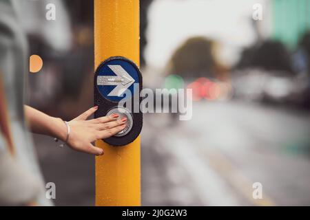 Pousser pour traverser en toute sécurité. Gros plan d'une femme appuyant sur un bouton à une promenade en croix. Banque D'Images