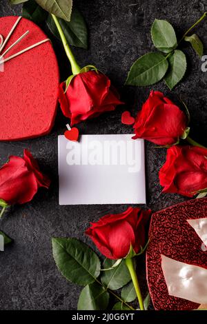 Boîte cadeau en forme de foyer rouge, roses, carte de message vide sur une table noire. Contexte de la Saint-Valentin. Banque D'Images