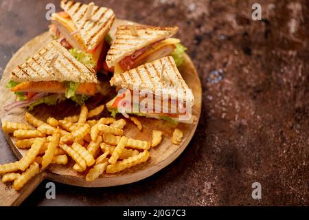 Des sandwiches au club de poulet et de fromage sont servis sur une planche de bois avec des frites Banque D'Images