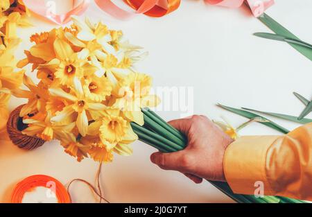 Homme tenant dans un bouquet de fleurs de jonquilles jaunes et rubans colorés avec corde sur fond blanc, vue de dessus Banque D'Images