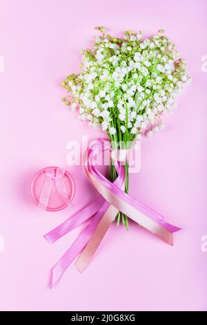 Un bouquet de lys de la vallée fleurit avec des rubans roses et une boîte rose avec des bijoux sur un fond rose gros plan Banque D'Images