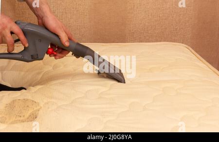 Un homme nettoie un matelas sale avec un aspirateur Banque D'Images