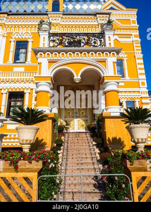 Bâtiment jaune avec ornements blancs, colonnes et une arche, portes avec un motif or et marches recouvertes de moquette Banque D'Images