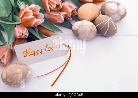 Carte de Pâques avec bouquet de tulipes et œufs colorés sur bois blanc . Banque D'Images