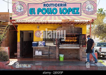 Un cuisinier se tient à côté de poulets tournant sur une broche dans un four de rôtisserie en façade pour El Pollo Lopez à San Carlos, Sonora, Mexique. Banque D'Images