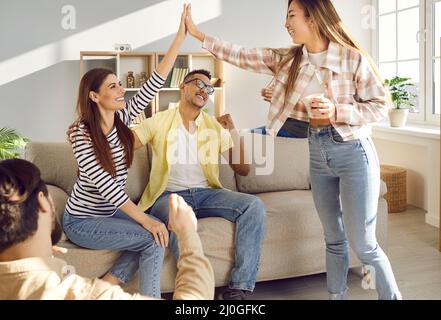 Les jeunes femmes enthousiastes et heureuses se donnent de fortes fiances tout en s'amusant à la maison avec leurs amis. Banque D'Images