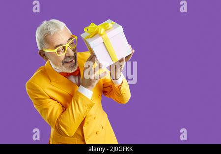 Joyeux drôle homme senior dans un costume jaune tenant une boîte présente d'une vente de vacances Banque D'Images