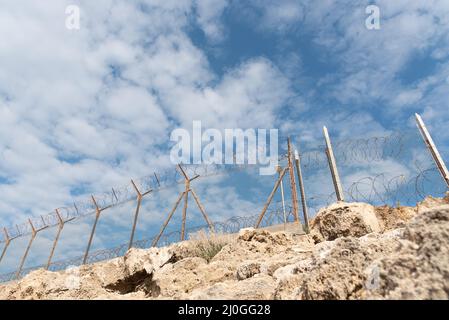 Clôture de sécurité avec fil barbelé contre un ciel bleu nuageux Banque D'Images
