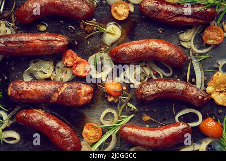 Vue de dessus sur de délicieuses saucisses grillées servies avec des oignons, des tomates, de l'ail, du pain et des herbes Banque D'Images